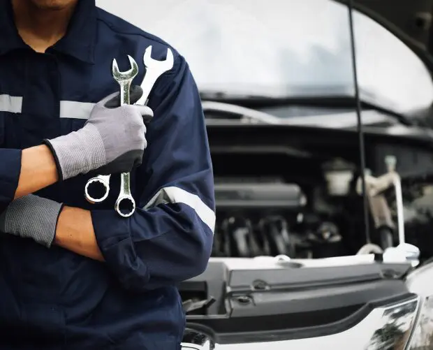 GettyImages-1387759698 Mechanic holding wrenches near open car hood.